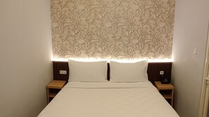 Una cama bien hecha con sábanas blancas, dos mesitas de noche con lámparas, y una pared con un diseño de árboles.