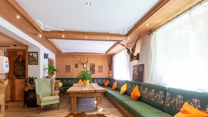 Ein Zimmer mit Holzboden, einem grünen Sofa mit orangen Kissen, einem Holztisch und einem Kuhfellteppich.