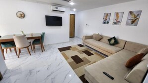 A modern living room with a sofa, a coffee table, and a TV mounted on the wall. - Elegant Furnished S1 With Security in Ariana - Tunisia (La Soukra)