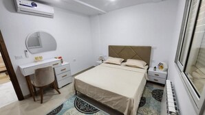 A bedroom with a bed, a desk, a chair, a mirror, and a radiator. - Elegant Furnished S1 With Security in Ariana - Tunisia (La Soukra)