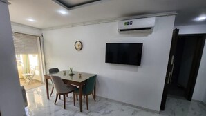 A dining area with a table and chairs, a flat-screen TV mounted on the wall, and an air conditioning unit. - Elegant Furnished S1 With Security in Ariana - Tunisia (La Soukra)
