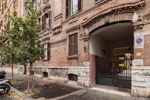 A historic building with a gated entrance, a tree, and a parked motorcycle.