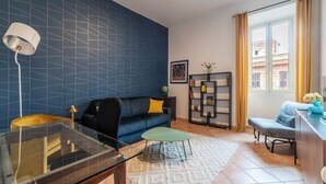 Ein Wohnzimmer mit blauer Fliesenwand, einer Couch, einem Couchtisch, einem Bücherregal und einem Fenster mit Vorhängen.