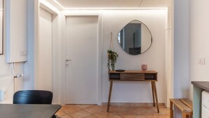 Ein modernes Interieur mit einer weißen Tür, einem runden Spiegel, einem Holztischchen mit Pflanze und einem schwarzen Stuhl.