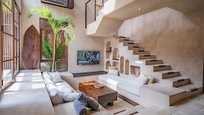 Un salon moderne avec un canapé, une table basse et un téléviseur. On y trouve un escalier au design original et une grande fenêtre offrant une belle vue.