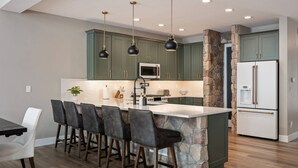 A kitchen with a central island, bar stools, a refrigerator, and a microwave. - Breathtaking Mountain Manor, Huge Deck w/ Hot Tub, Everything High End and New, 1 Mile to Ski Slopes (Granby)