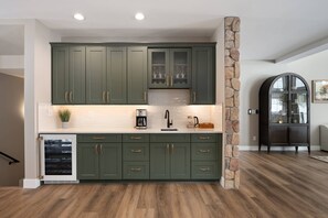 A modern kitchen with green cabinets, a stone accent wall, and a built-in refrigerator.