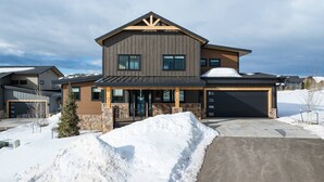 A two-story house with a stone foundation, a garage, and a covered porch. - Breathtaking Mountain Manor, Huge Deck w/ Hot Tub, Everything High End and New, 1 Mile to Ski Slopes (Granby)