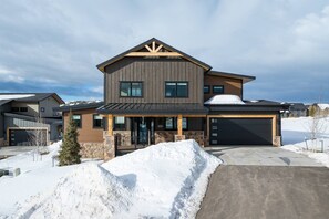 Une maison à deux étages avec des fondations en pierre, un garage et une véranda couverte.