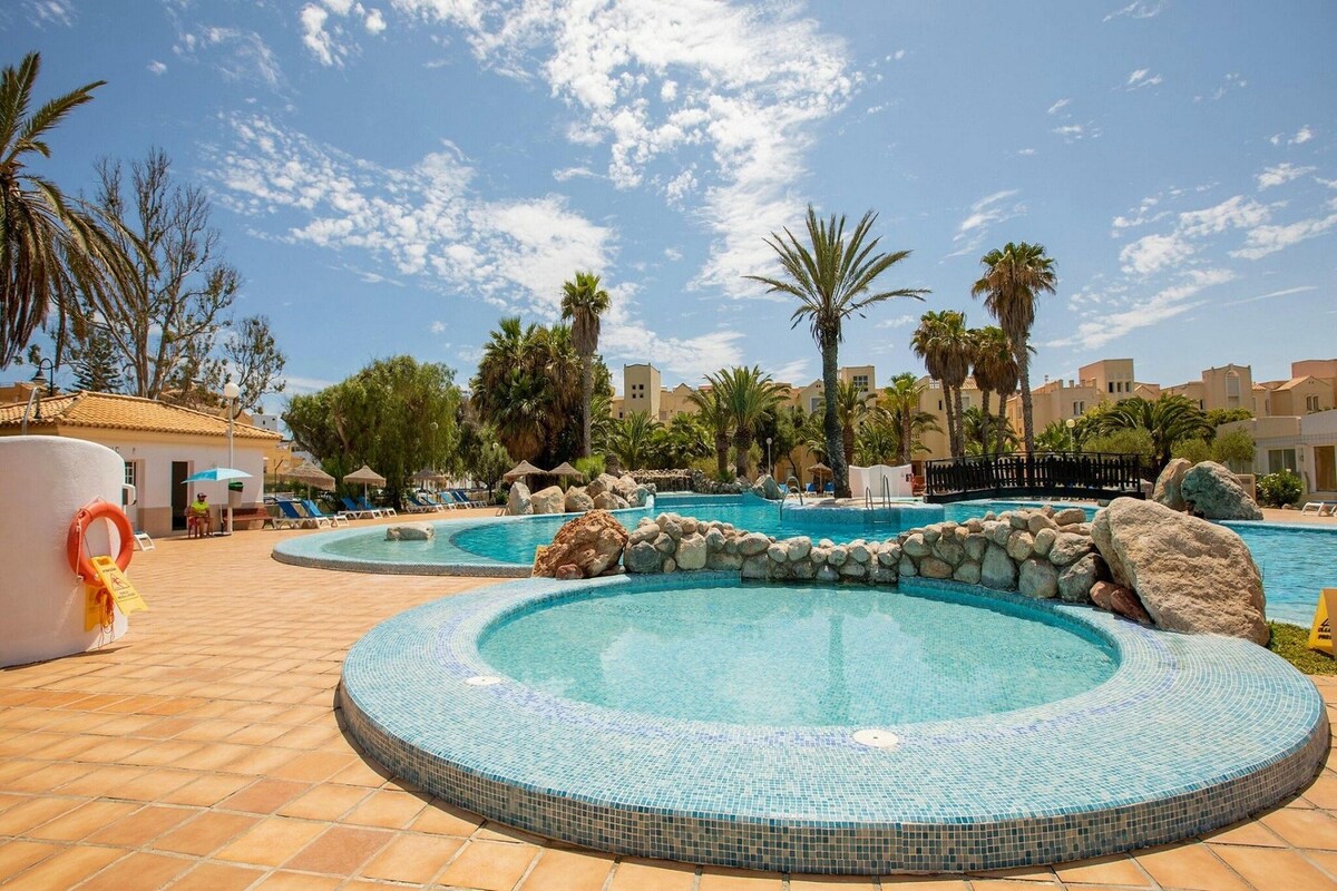 A pool area with multiple swimming pools, palm trees, and a clear sky.