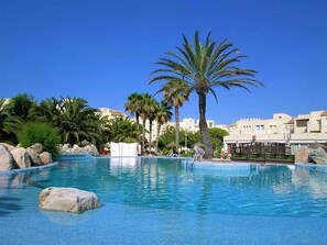 A clear blue pool with palm trees and rocks, surrounded by buildings. - Lively Apartment With Large Pool (Roquetas de Mar)
