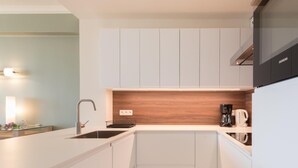 A modern kitchen with white cabinetry, a wooden backsplash, and a built-in microwave. - Apartment With Marina View (Ostend)