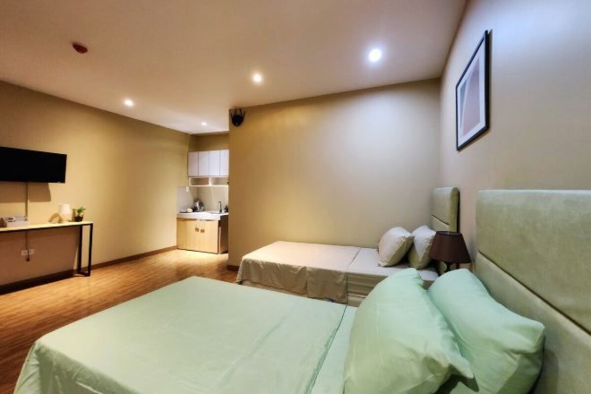 A hotel room with two beds, a desk, a TV, and a kitchenette.