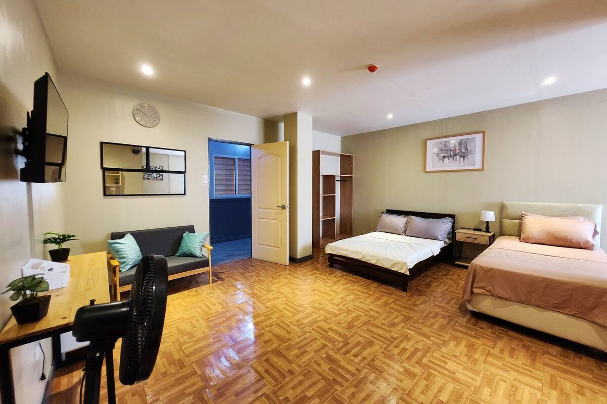 Une pièce spacieuse avec un plancher en bois, un lit, un bureau avec une chaise, un canapé, une armoire et un miroir.