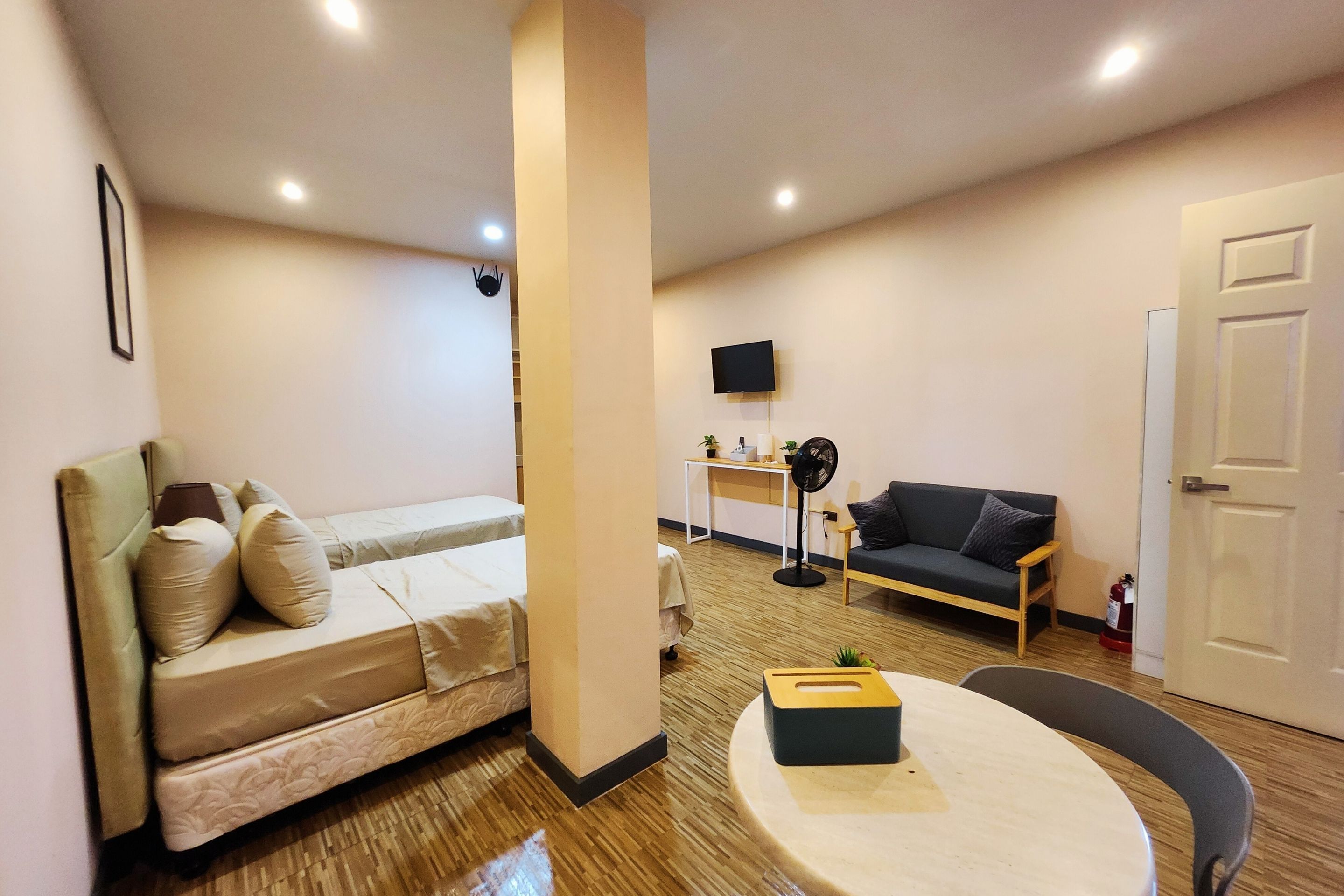 Un espacio habitable pequeño con cama, sofá, una mesita, televisor y una puerta.