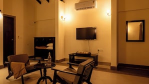 A cozy living room with a sofa, armchair, and coffee table, a flat-screen TV mounted on the wall, and a small table with a bottle and glasses. - Amora A Boutique Resort (Paud)