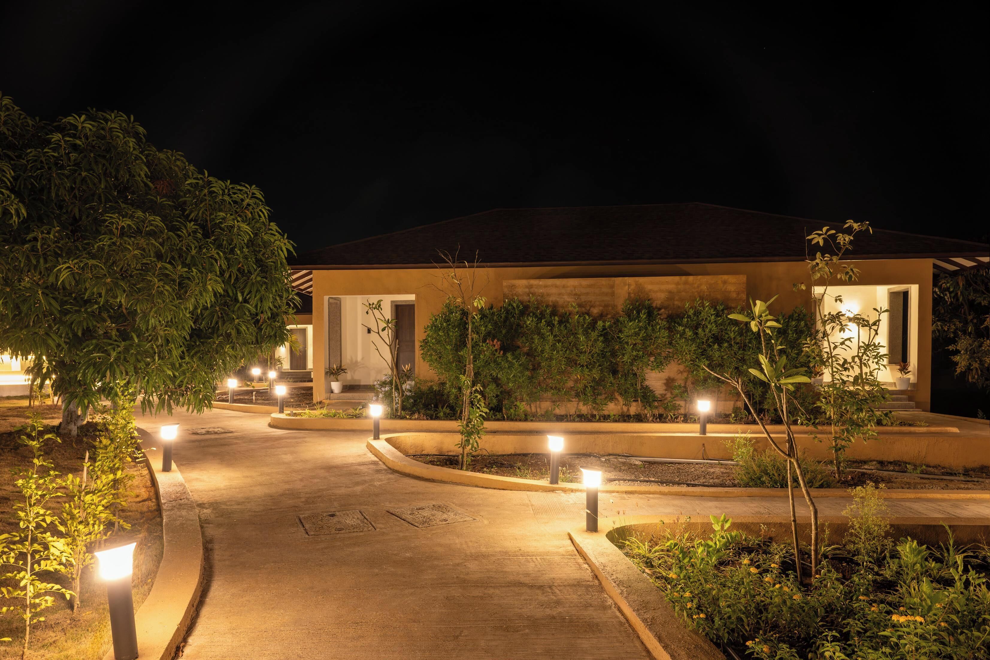 A well-lit pathway leading to a building with a curved driveway and landscaped areas.