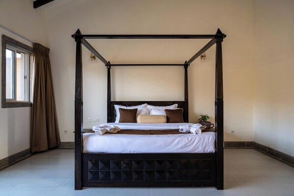 A four-poster bed with a dark wooden frame, white bedding, and a small potted plant on the nightstand. - Amora A Boutique Resort (Paud)
