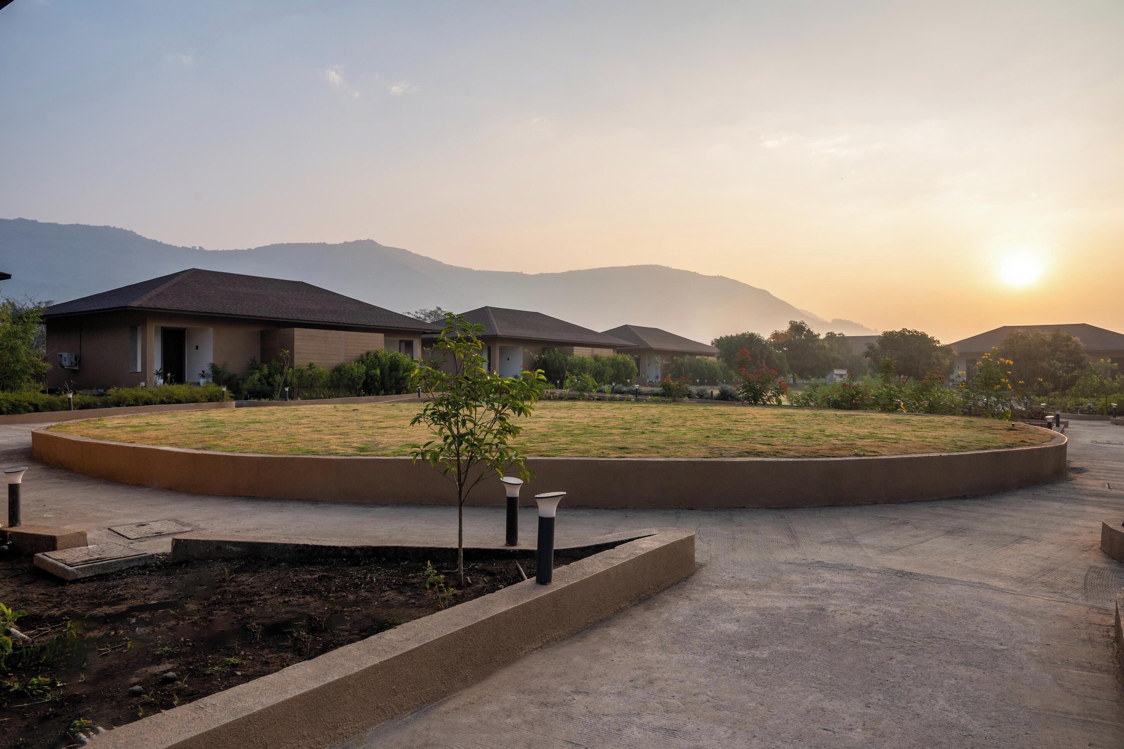 A residential area with houses, a circular landscaped garden, and mountains in the background.