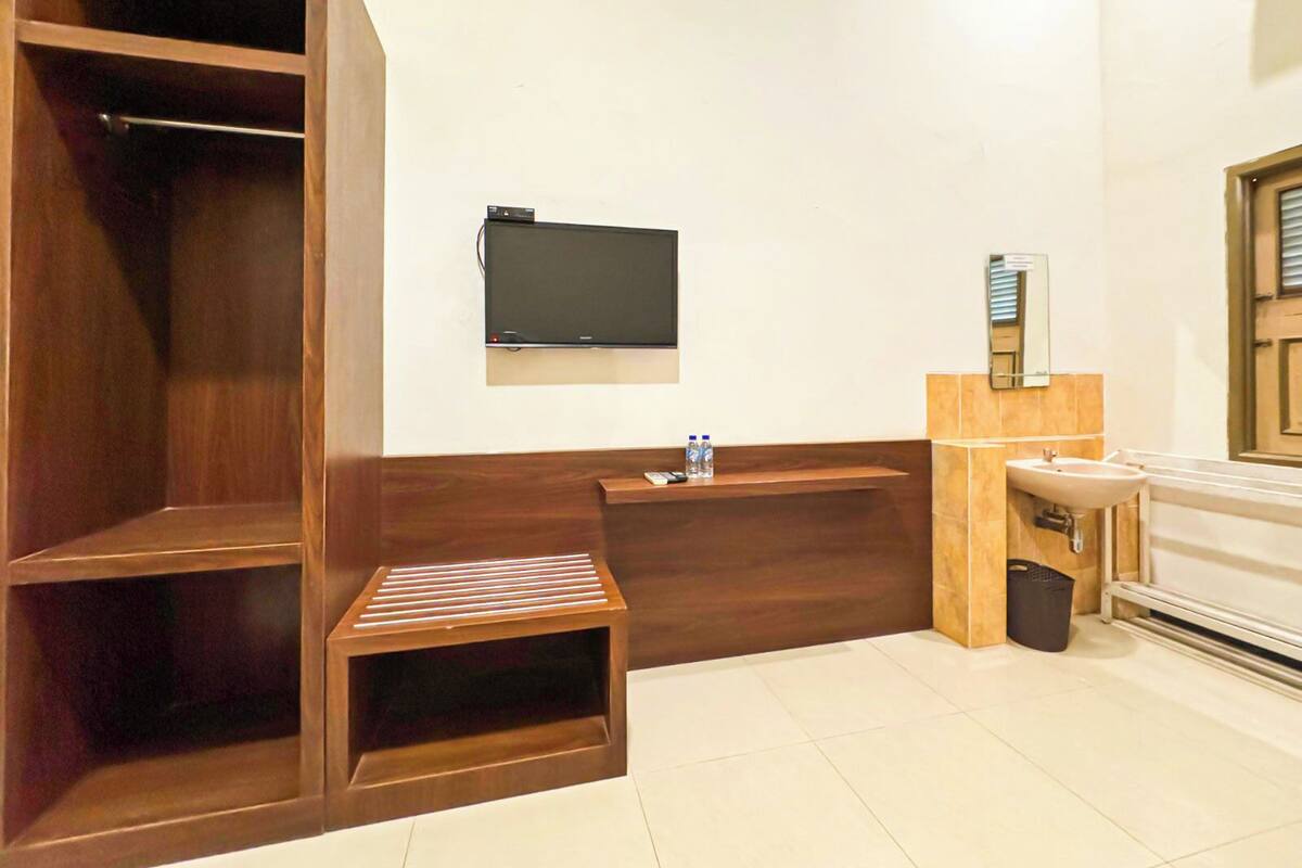 Een moderne badkamer met een houten wastafelmeubel, een wastafel, een spiegel en een aan de muur bevestigde televisie.