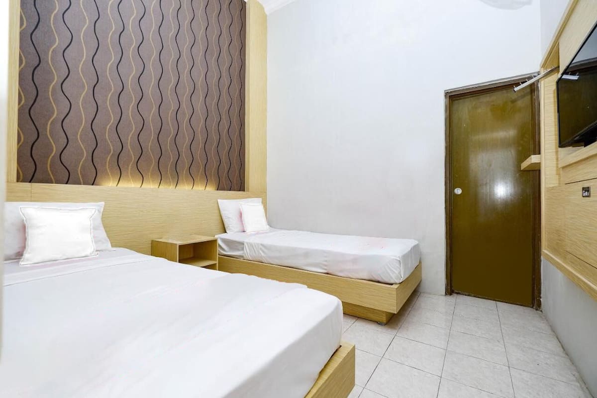 Een hotelkamer met twee eenpersoonsbedden, een houten hoofdbord, een klein nachtkastje en een garderobe.