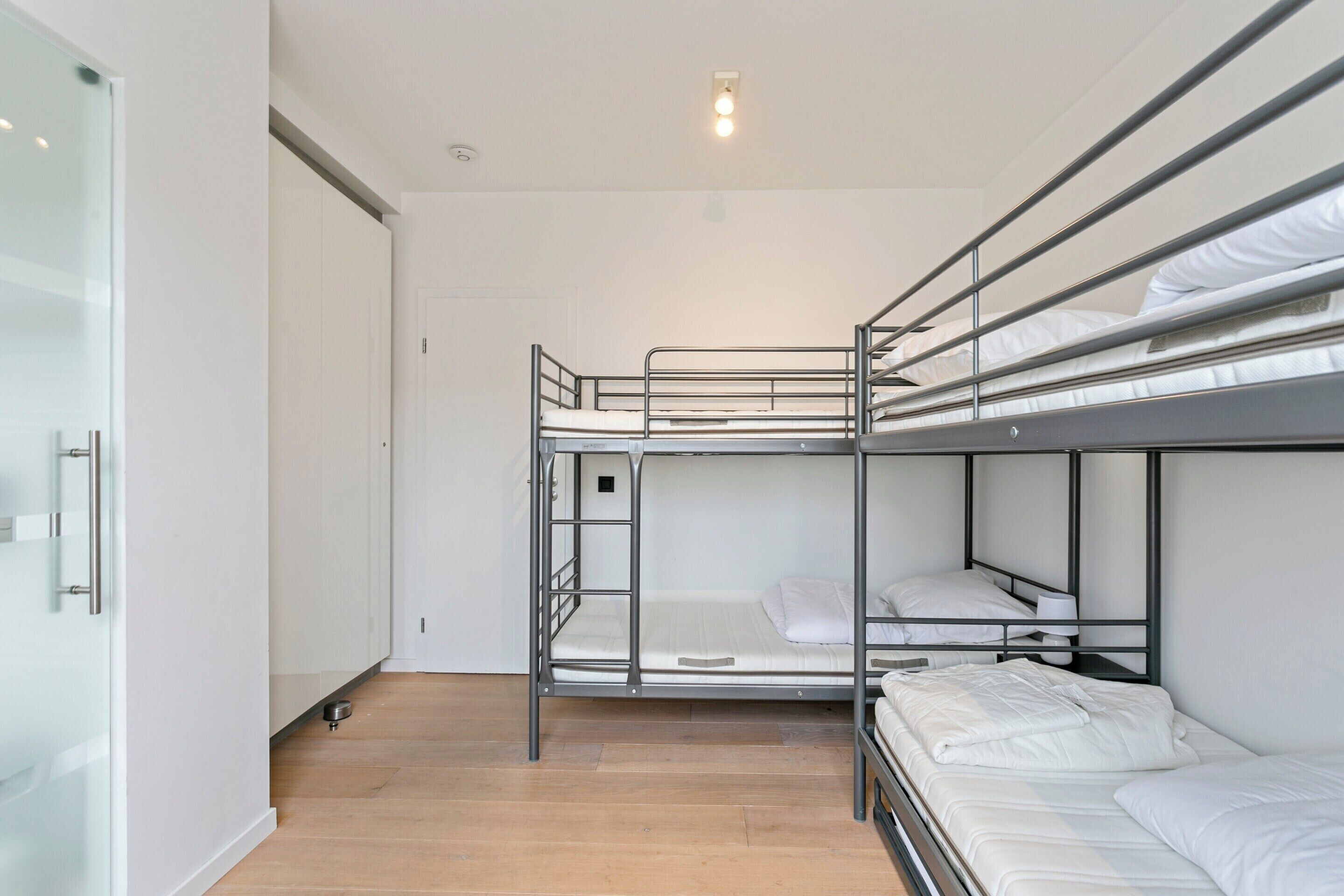 A bunk bed room with white bedding, a wooden floor, and a white door.