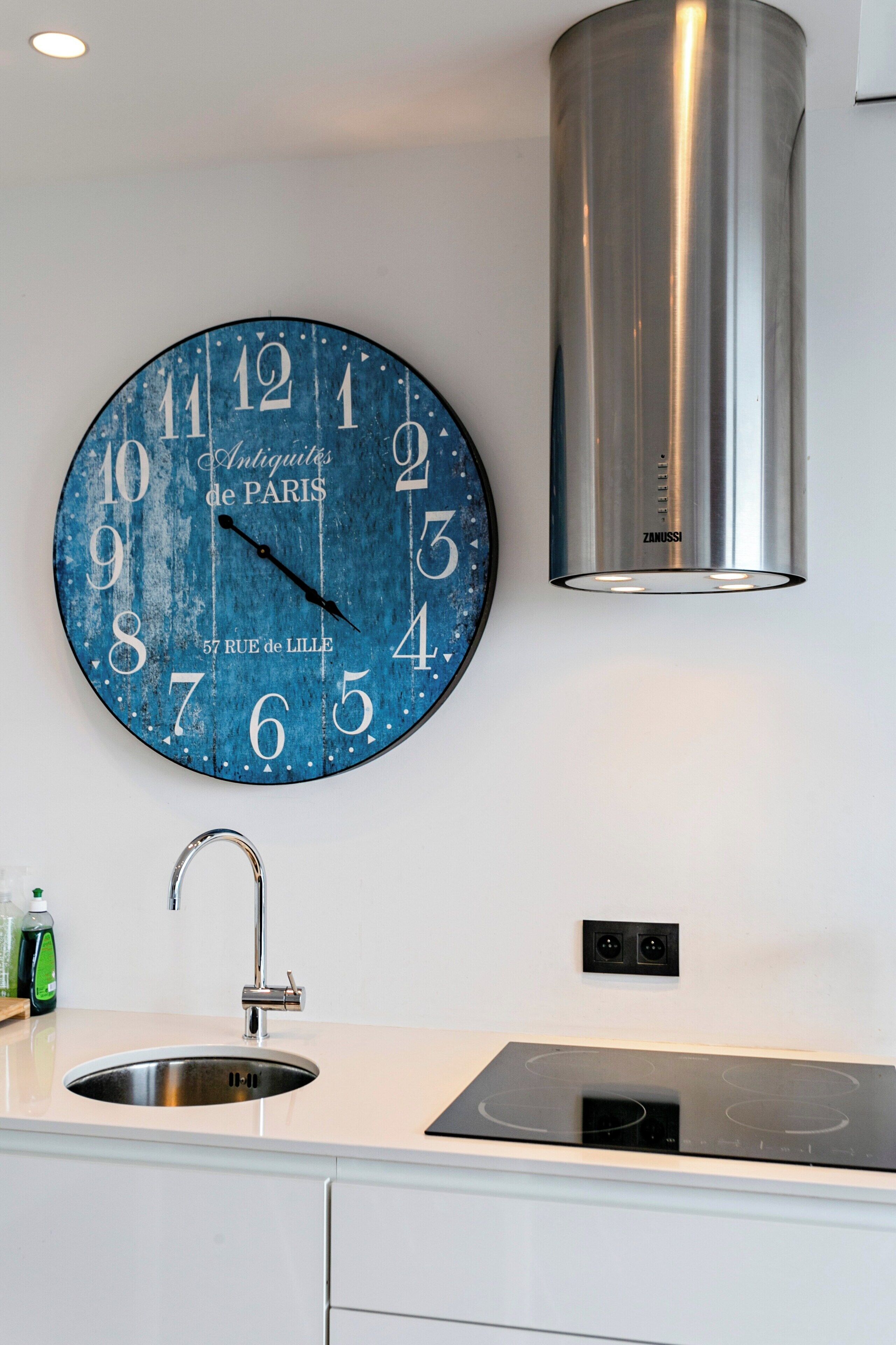 A kitchen with a round wall clock, stainless steel sink, and a modern stove.