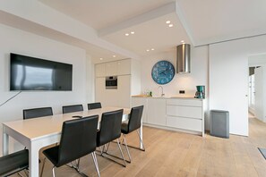 A modern kitchen with a clock, a dining area with chairs, and a TV mounted on the wall. - Penthouse in Blankenberge Near the Beach (Blankenberge)