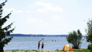 Ein Strand mit einem Zelt und zwei Personen am Wasser.