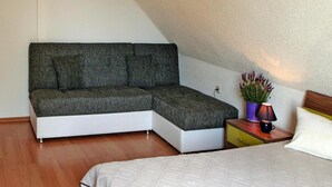 Ein Schlafzimmer mit einem Bett, einer Eckcouch, einem Nachttisch mit Lampe und einer Topfpflanze.