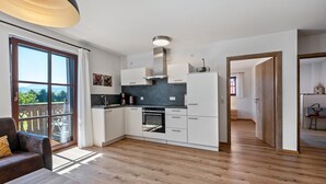 A modern kitchen with white cabinetry, a built-in oven, and a large window offering a view of the outdoors. - Apartment 'Untersbergblick' with Mountain View, Balcony and Wi-Fi (Freilassing)