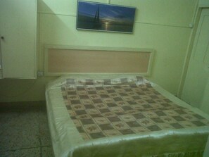 Een kleine, eenvoudige kamer met een bed, een aan de muur bevestigde televisie en een effen muur.