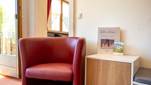 Une chaise rouge, un meuble blanc avec une porte en bois, et un livre encadré intitulé « Noël chez les Wilking » accroché au mur.