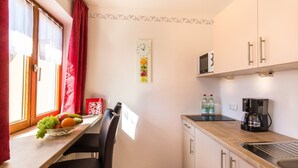 Une petite cuisine avec un plan de travail en bois, un four à micro-ondes, une machine à café et un panier de fruits posé sur la table.