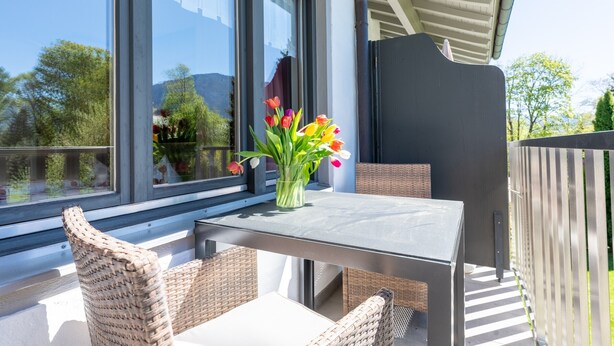 Un balcon avec des fauteuils en osier, une table et un vase de fleurs.