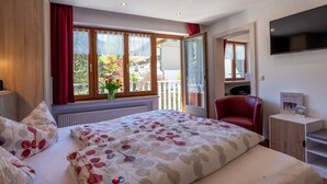 Une chambre d’hôtel avec un lit, une chaise rouge, une télévision et un balcon avec vue.
