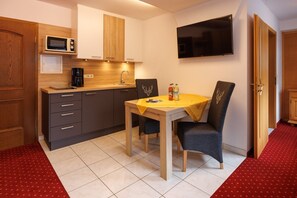 A compact kitchen with a microwave, coffee maker, and a dining table with chairs.
