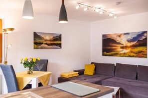 Un salon moderne avec un canapé, une table à manger agrémentée d’un vase de fleurs et deux tableaux accrochés au mur.
