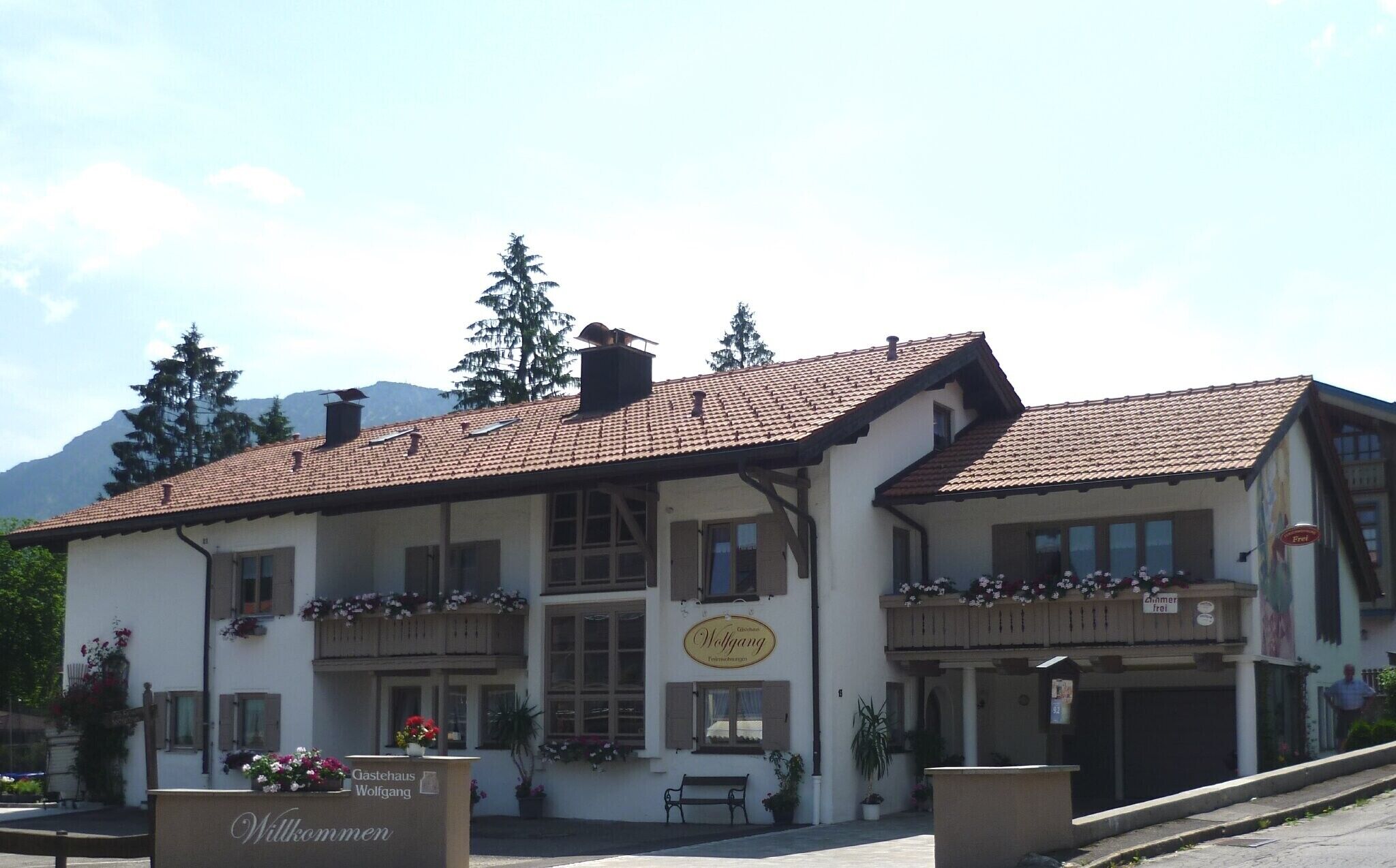 A two-story building with a sign 'Gastehaus Wolfgang' and a bench outside.