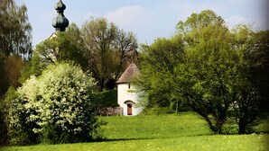 Ein kleines, weißes Gebäude mit roter Tür, umgeben von üppigem Grün und Bäumen.