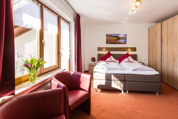 Ett hotellrum med en säng, ett skrivbord, en stol, ett fönster med gardiner och en tavla på väggen.