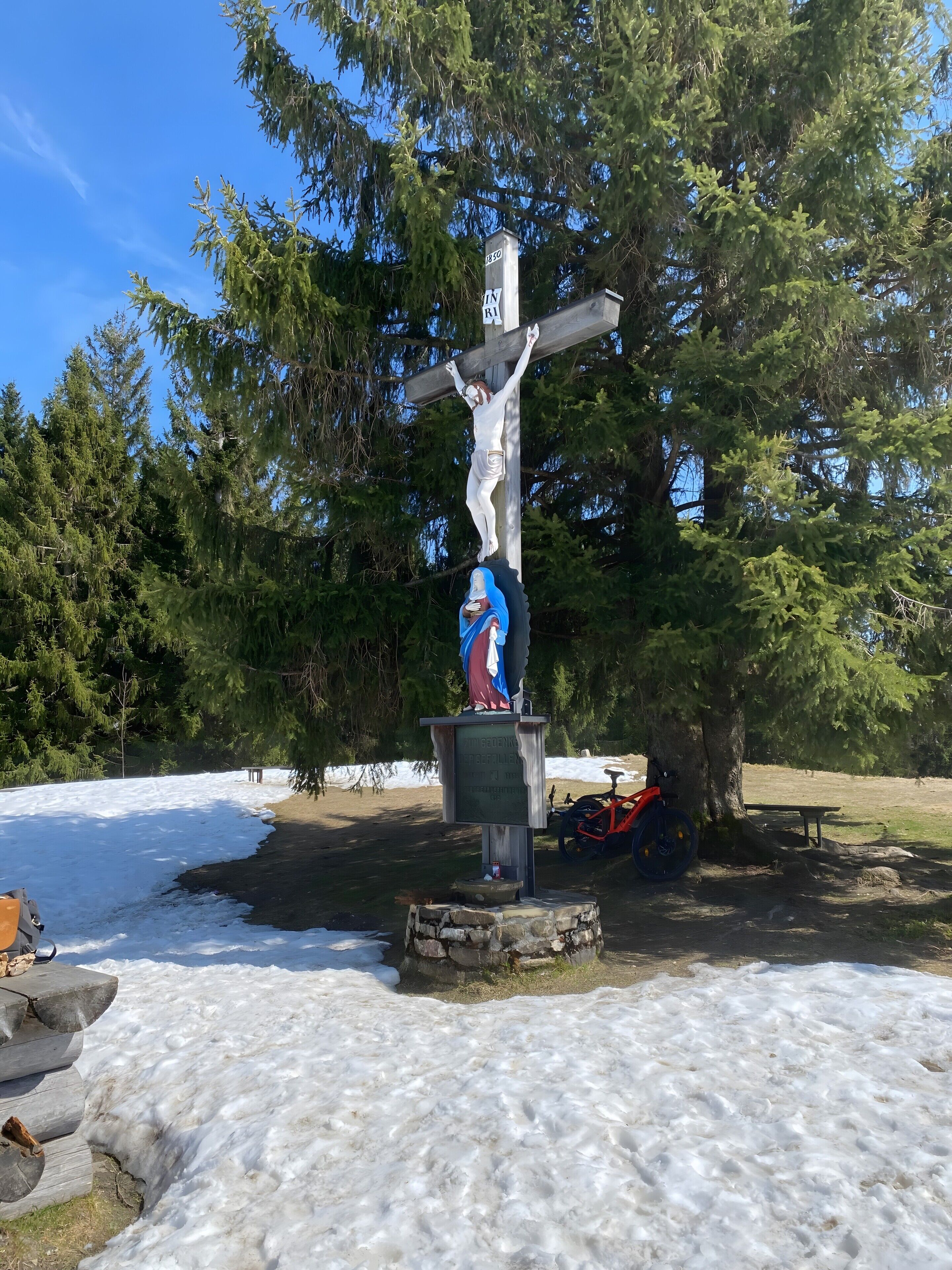 A wooden cross with a figure, surrounded by snow and trees.