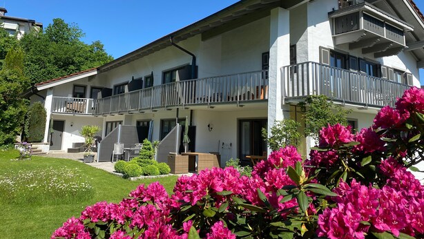 A two-story building with balconies, a garden, and a clear blue sky.
