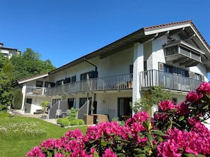 A two-story building with balconies, a garden, and a clear blue sky. - Studio Apartment 'Gästehaus Wolfgang Mittersee -4-' with Mountain View, Balcony and Wi-Fi (Ruhpolding)