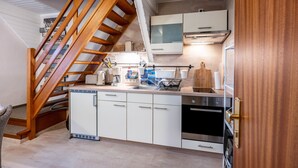 Una cocina con armarios blancos, lavavajillas, estufa y escalera de madera.