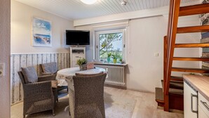 Una habitación con muebles de mimbre, televisor, ventana con vistas y una escalera de madera.
