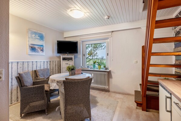 A room with wicker furniture, a television, a window with a view, and a wooden staircase.