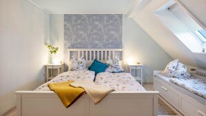 Un dormitorio con techo inclinado, una cama con ropa de cama floral, una mesita de noche con una lámpara y una ventana con vistas.