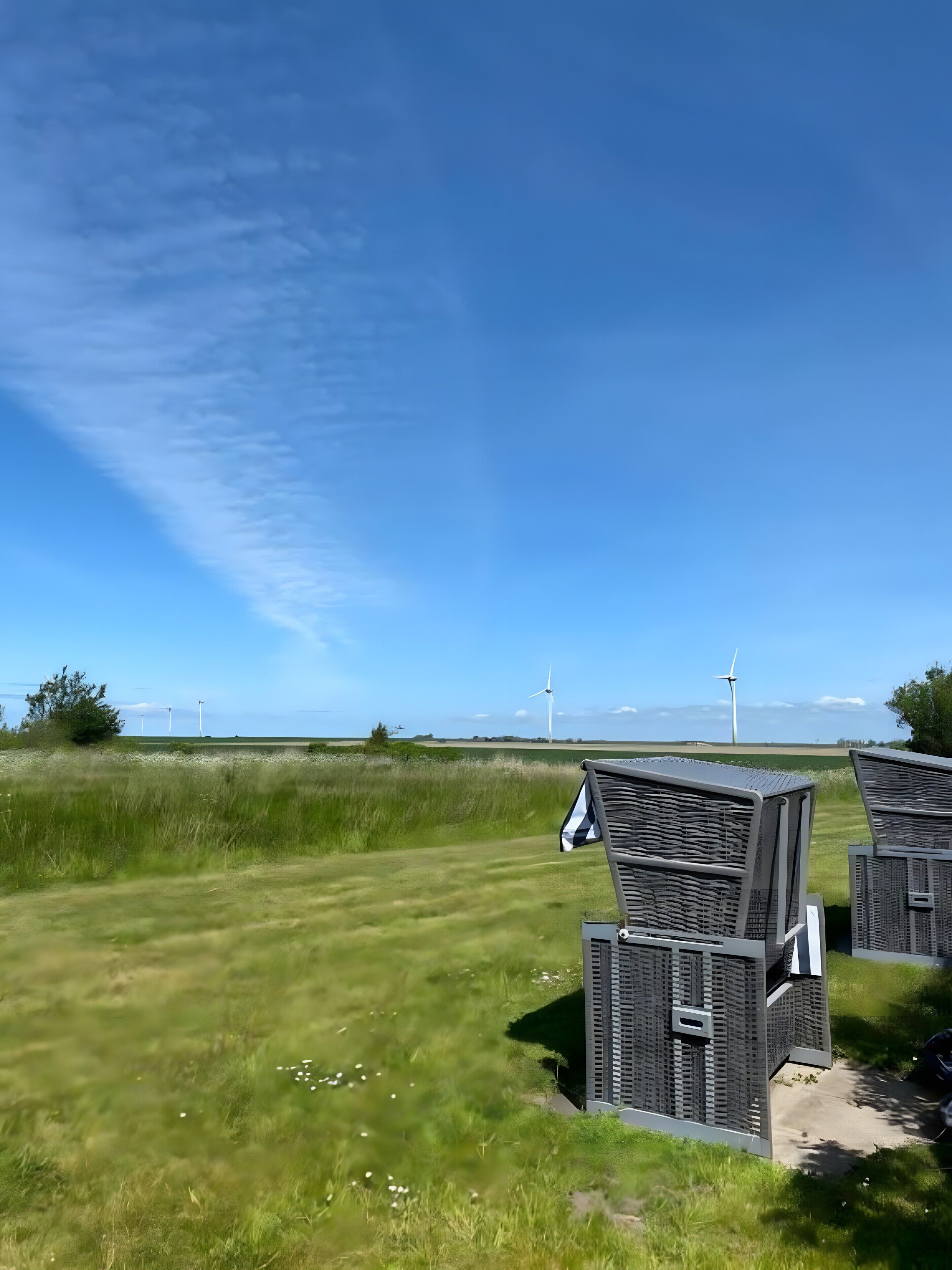 A grassy field with wind turbines in the distance and two outdoor seating areas.