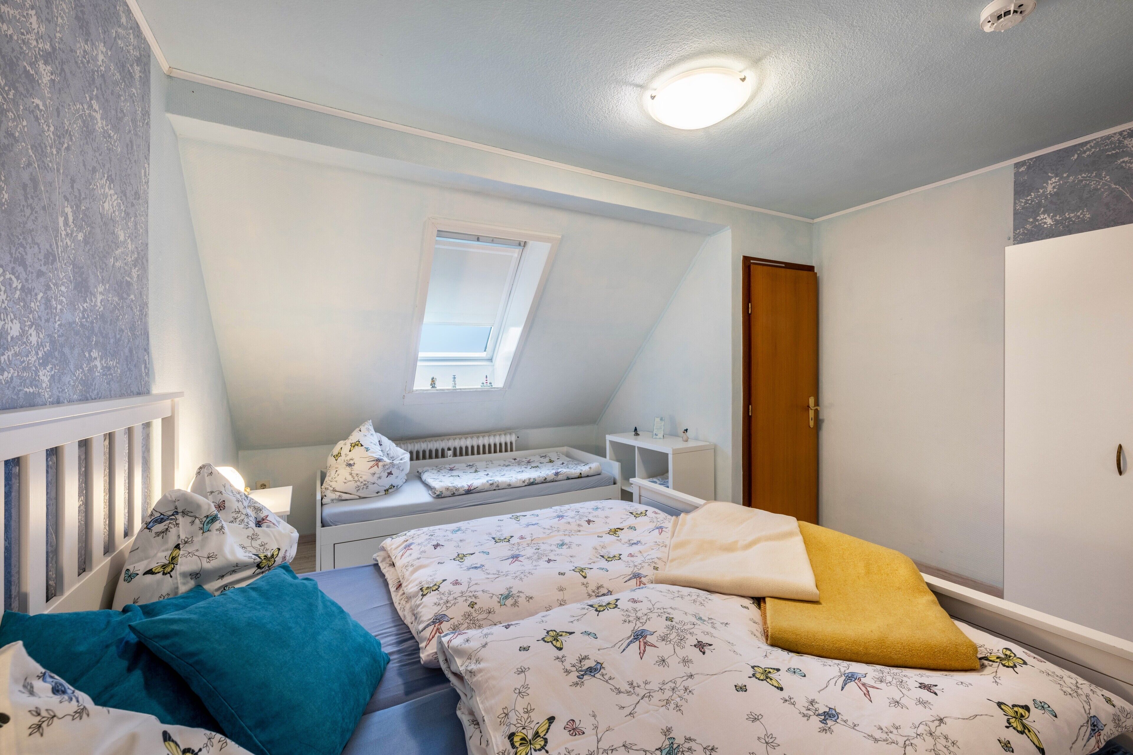Slaapkamer met schuine wand, dakraam, ledikant, bed met bloemenprint beddengoed en een kledingkast.